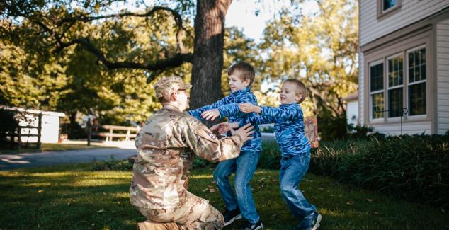 Man in camo fatigues about to hug two children on a lawn