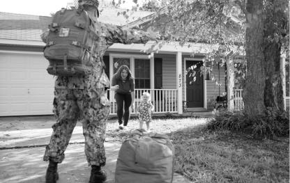 A soldier and family greet each other in front of a house