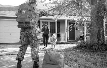 A soldier and family greet each other in front of a house